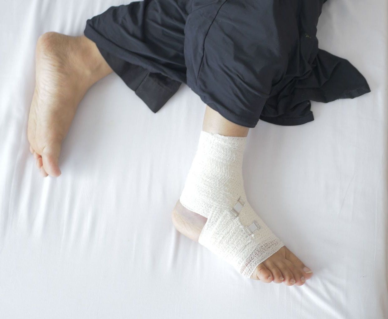 Top view of a bandaged foot resting on a bed, depicting injury and recovery.